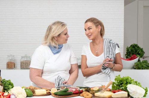 Two women in a kitchen preparing fresh vegetables and cheese with olive oil and spices.